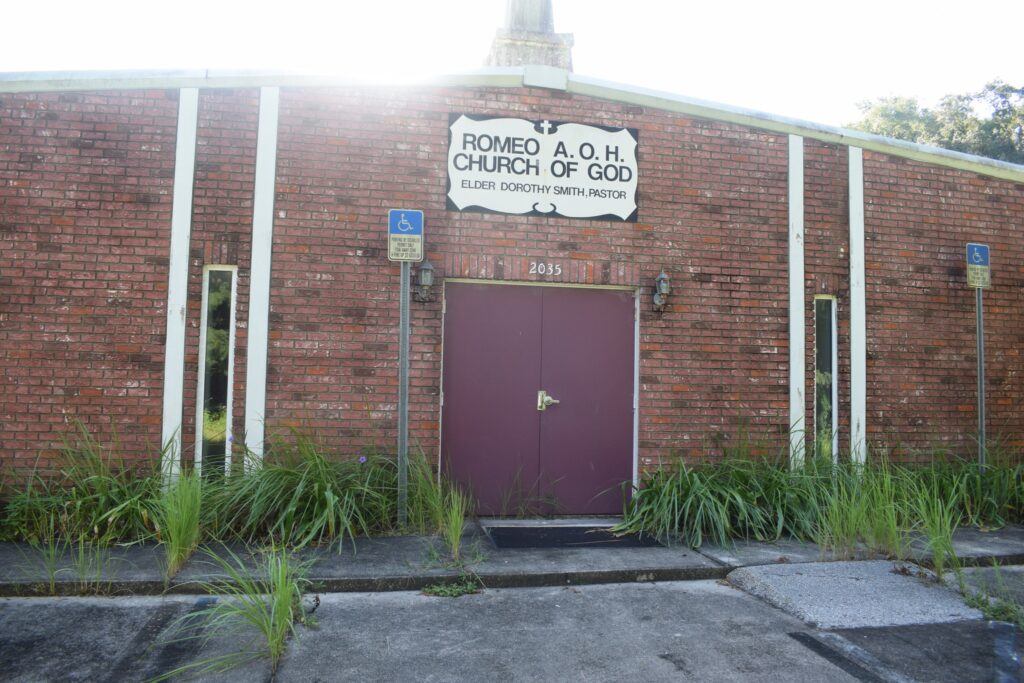 Brick Romeo A.O.H. Church of God surrounded by overgrown vegetation in Romeo, Florida