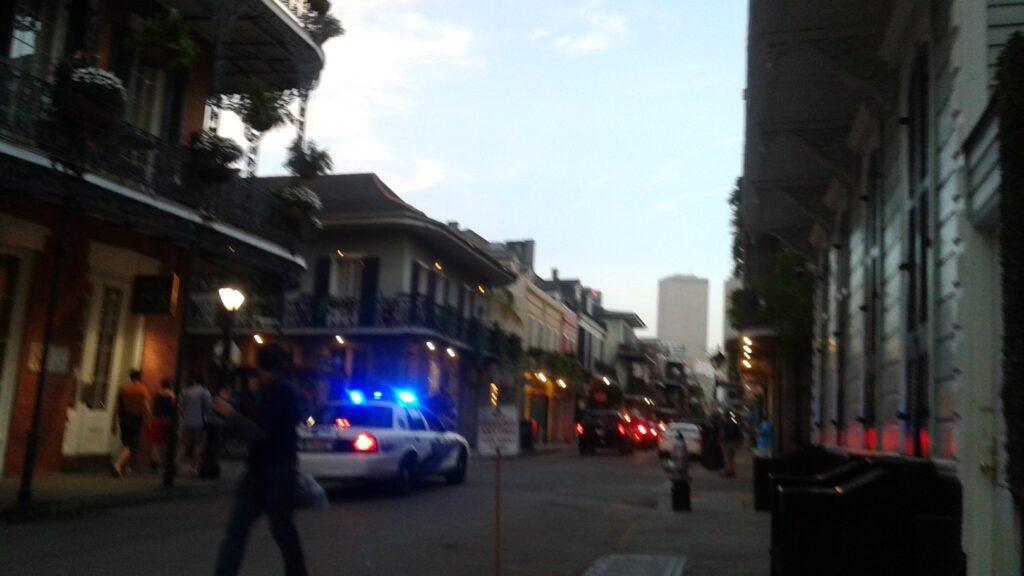 Crowded French Quarter street at night with police car lights and people walking along Royal Street in New Orleans.