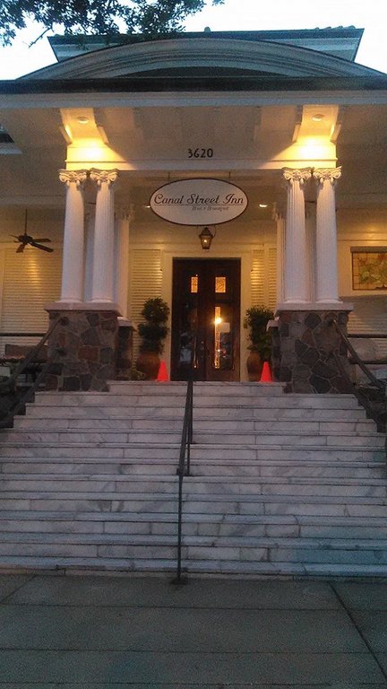 The Canal Street Inn glowing at dusk — a century-old mansion where New Orleans history hums right through the porch rails.