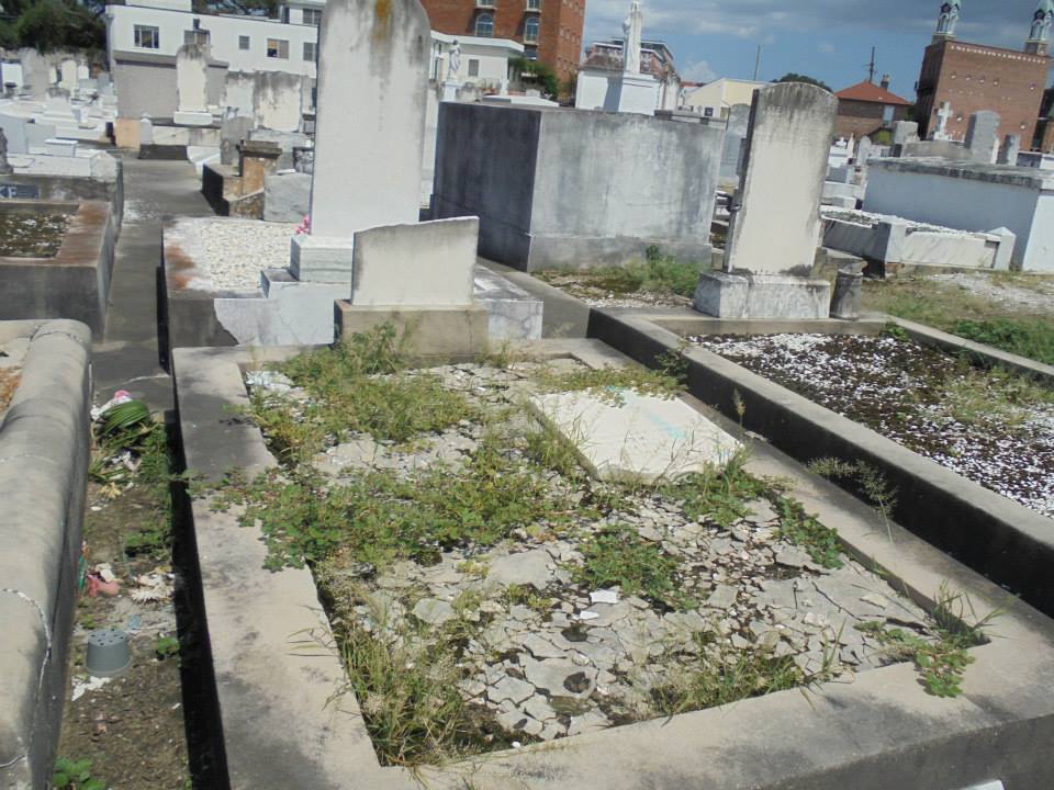 A cracked and weather-worn above-ground tomb showing storm damage, likely from Hurricane Katrina, with faded marble and missing plaster.
