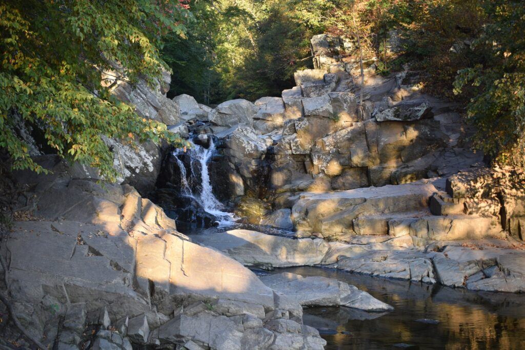 Close-up view of the waterfall at Scott’s Run, with water flowing over a wide rock ledge framed by rugged cliffs.