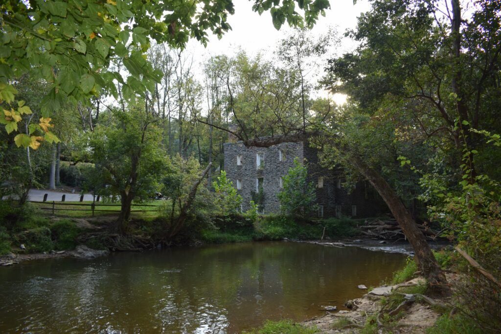 Abandoned Black Rock Mill reflected in the creek, its weathered stone walls half-hidden by trees in Seneca Creek State Park.