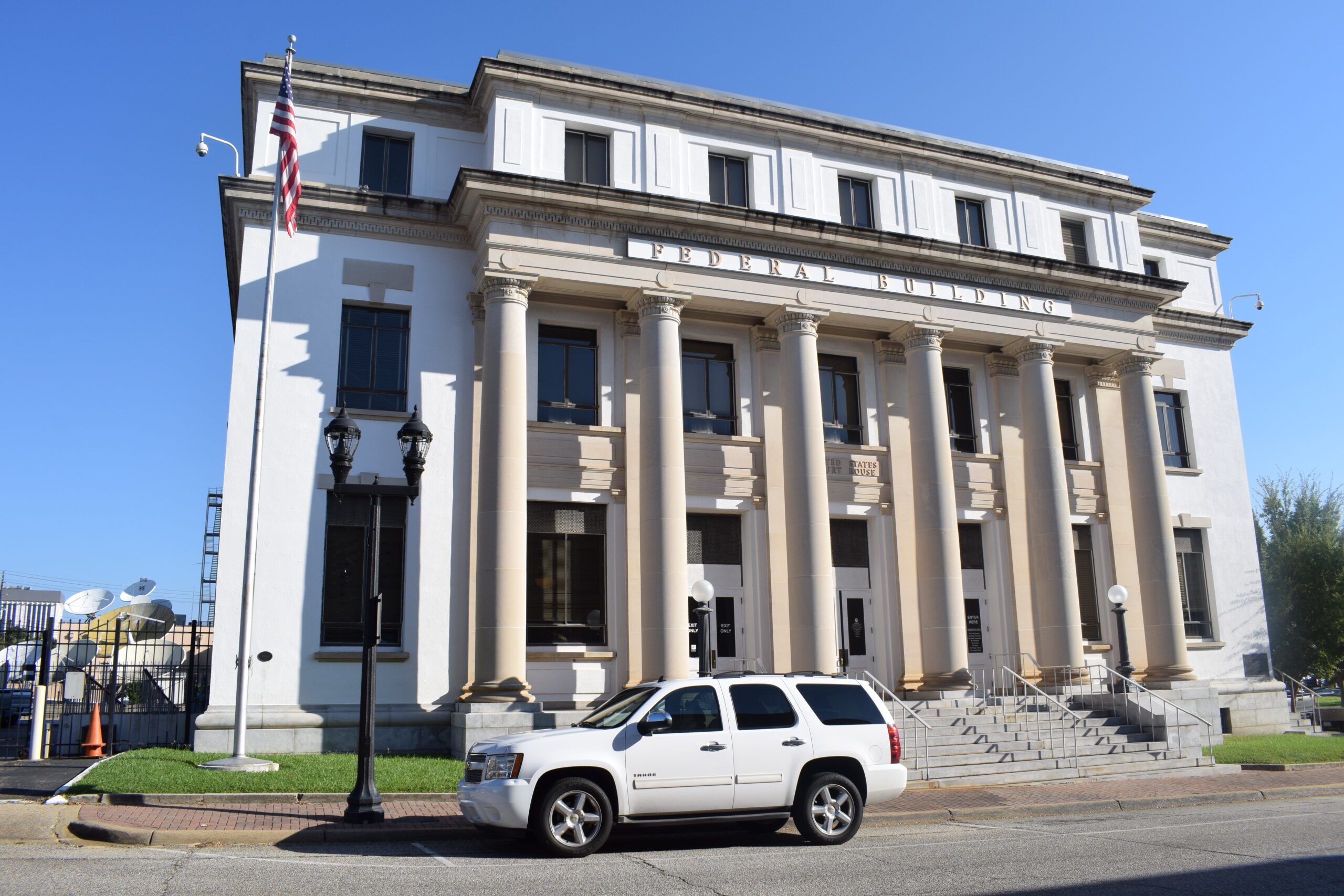 Front view of the Dothan Federal Building showing its six tall Doric columns, granite steps, and Classical Revival façade under a bright Alabama sky.