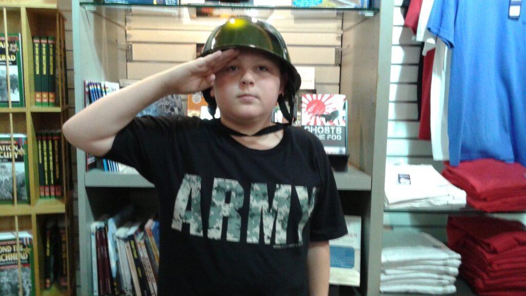 Boy wearing a camo helmet and Army t-shirt giving a serious salute inside the National WWII Museum gift shop in New Orleans.