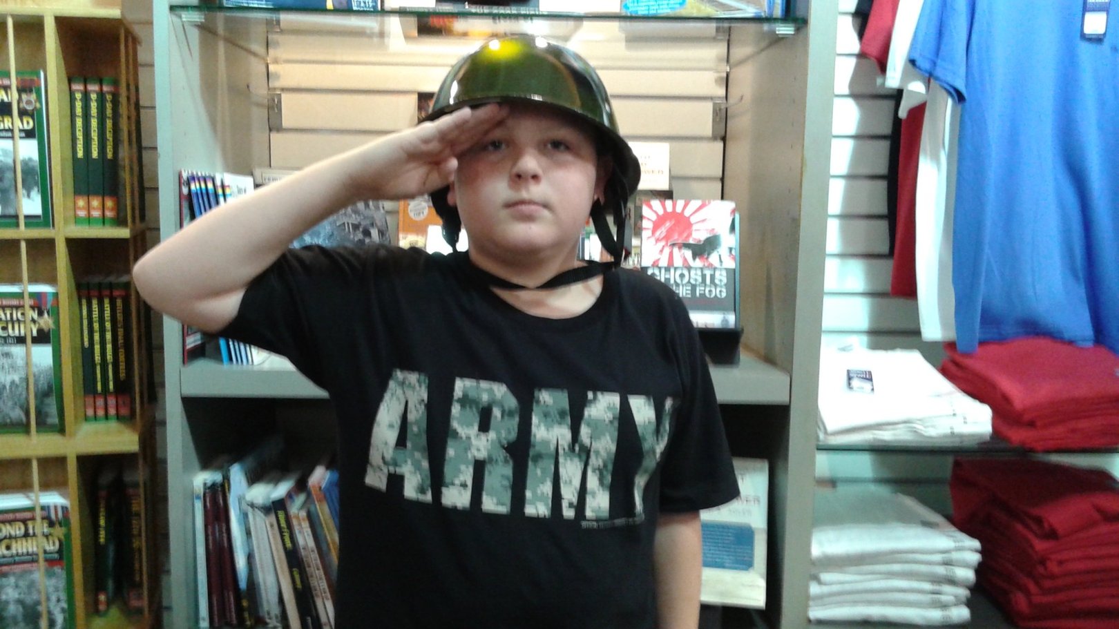 Boy wearing a camo helmet and Army t-shirt giving a serious salute inside the National WWII Museum gift shop in New Orleans.