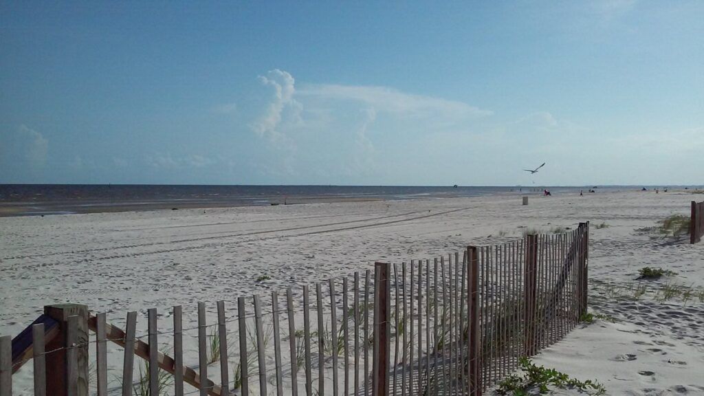 Weathered wooden sand fence leading across white sand dunes at Pass Christian Beach on the Mississippi Gulf Coast.
