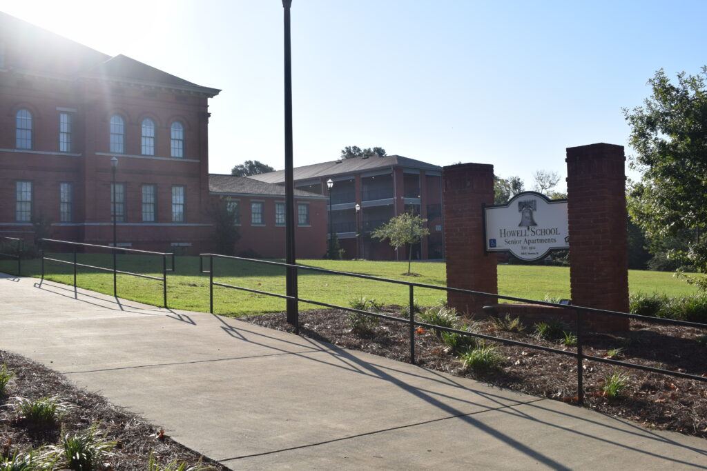 Howel School Senior Apartments sign with old school building and apartment building in the background.
