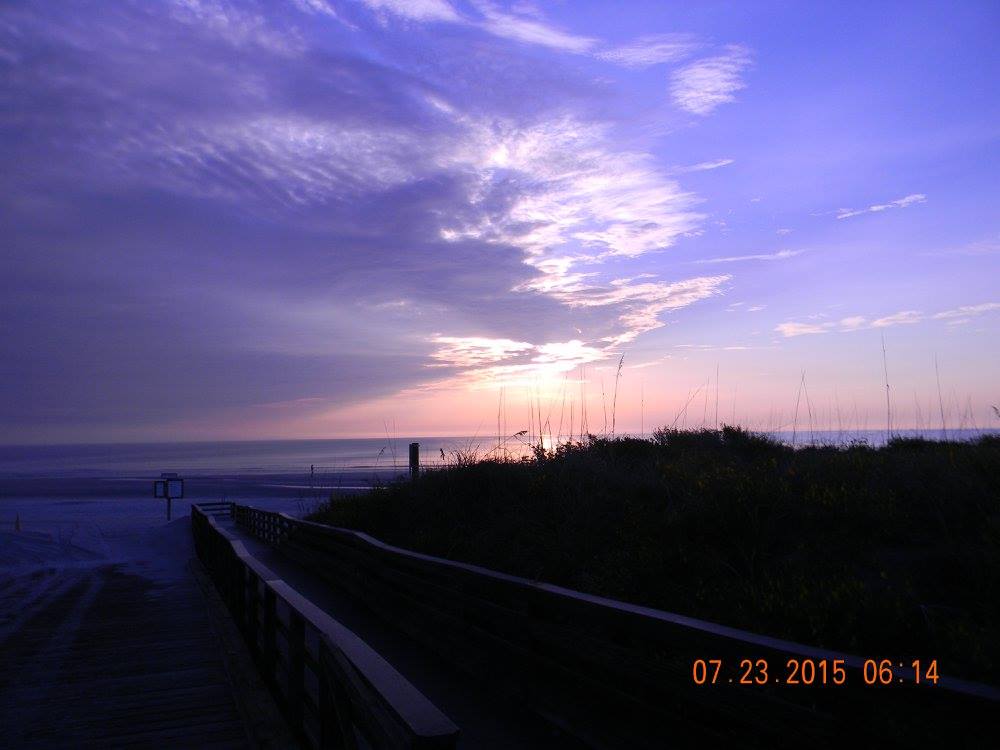 Sunrise over the Atlantic Ocean at Crescent Beach Park in Florida, with soft purple and gold light reflecting across the waves and shoreline.