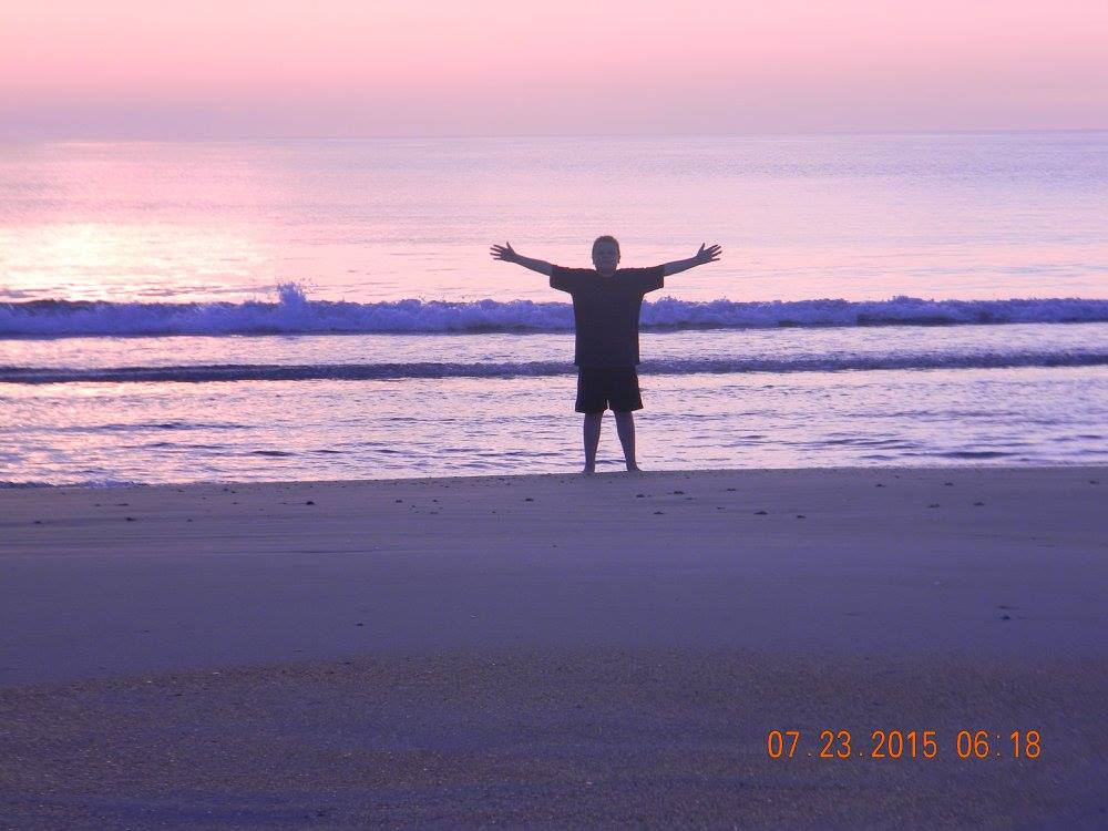 A child standing on Crescent Beach at sunrise with arms spread wide as early morning light fills the sky.