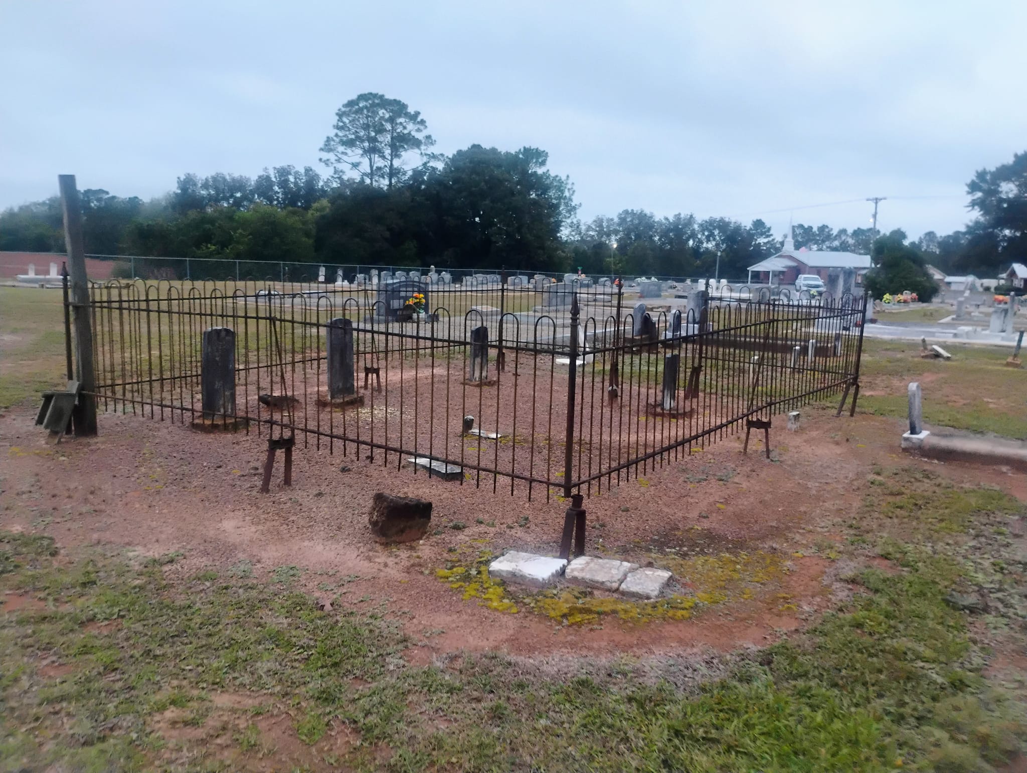 Historic fenced burial plot at Camp Springs Cemetery in Henry County, Alabama, with weathered headstones and rural Wiregrass landscape under an overcast sky.