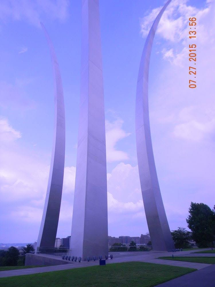 Three stainless steel spires of the United States Air Force Memorial rising into a blue sky with scattered clouds, viewed from below in Arlington, Virginia.