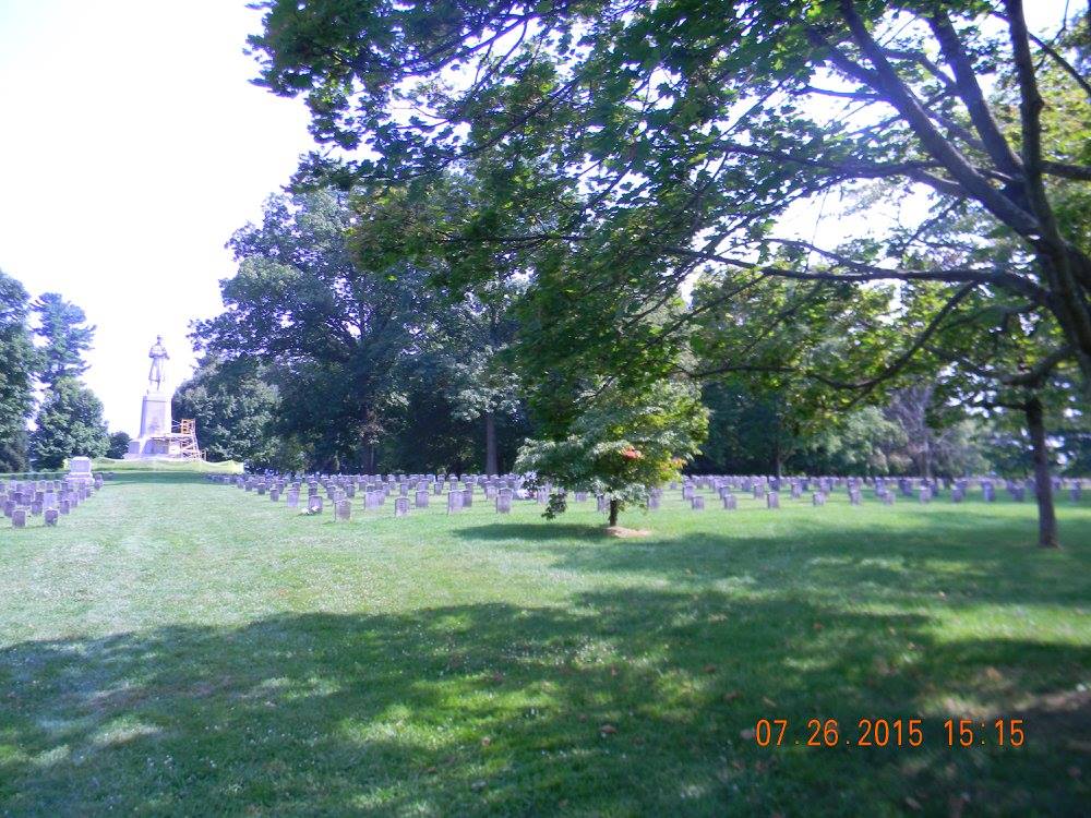 Peaceful view of Antietam National Cemetery with rows of white headstones stretching beneath trees and the “Old Simon” monument standing watch in the distance
