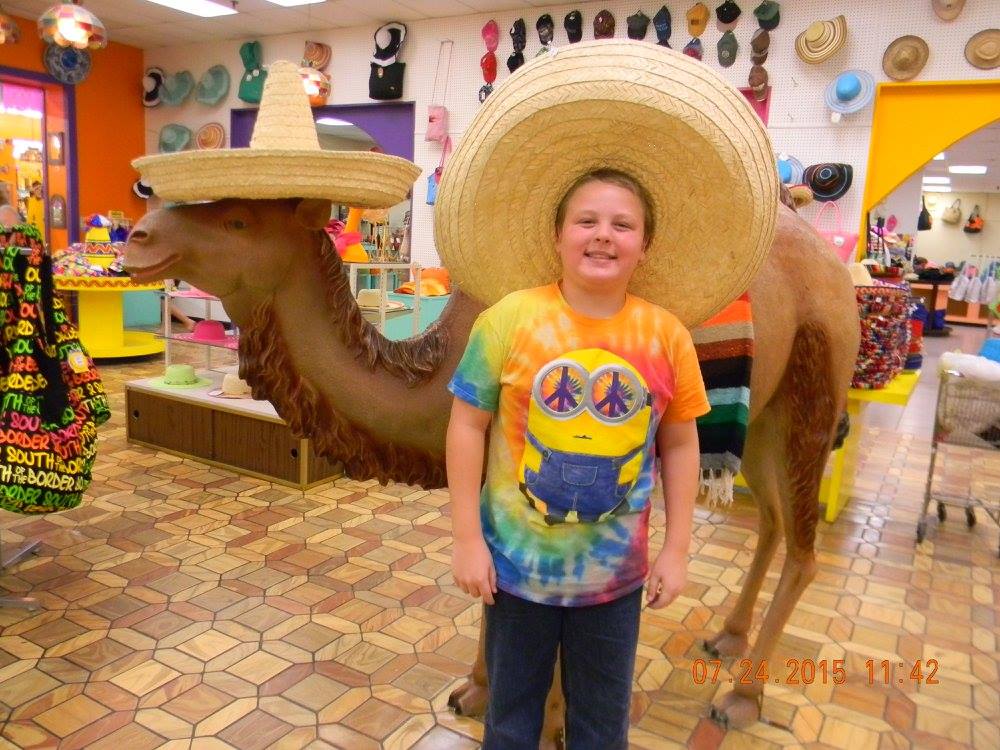 Smiling boy standing beside a camel statue wearing a sombrero inside South of the Border gift shop in South Carolina