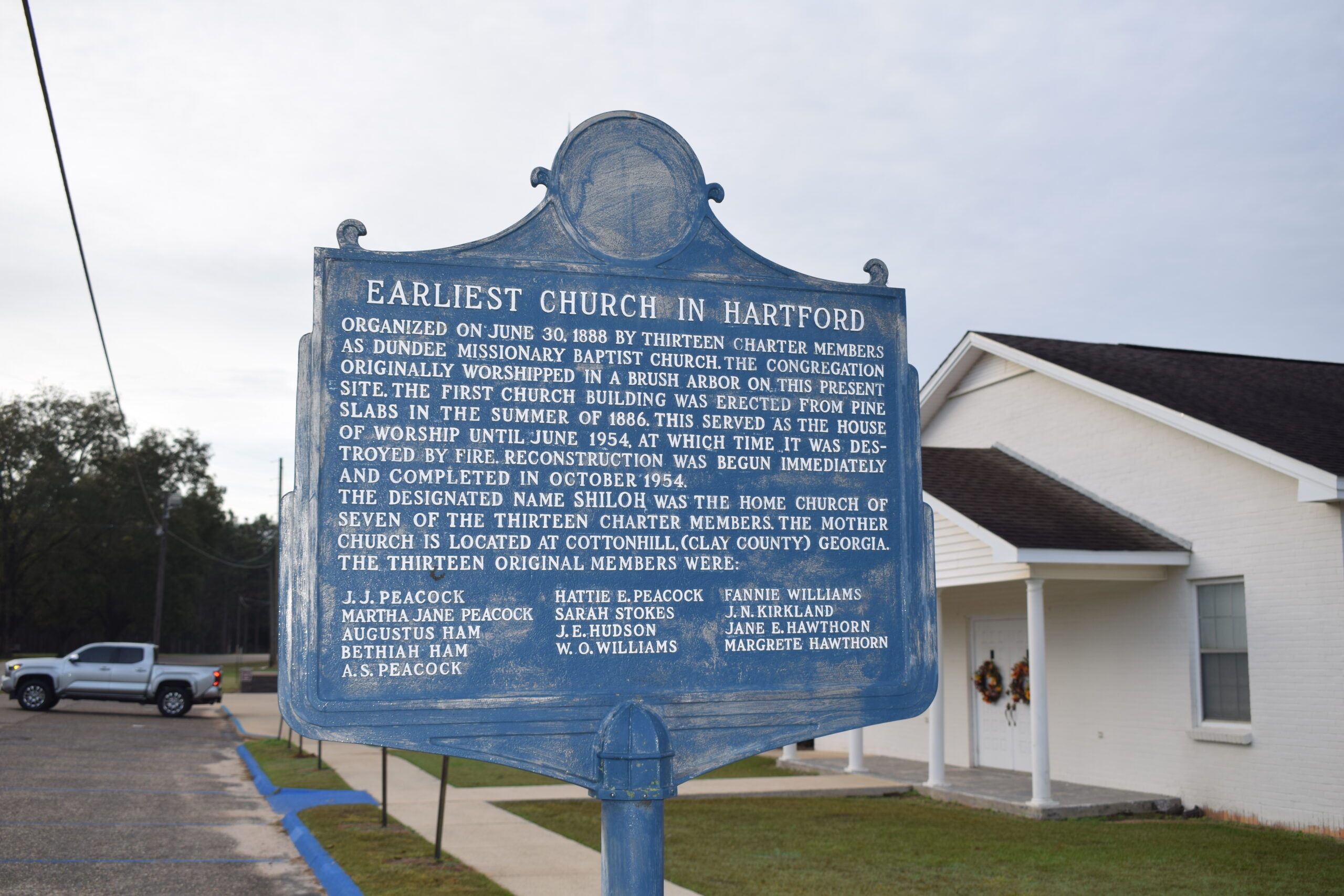 Weathered blue historical marker at Shiloh Baptist Church in Hartford, Alabama, telling the story of the town’s earliest church as it stands quietly beside the modern white chapel.