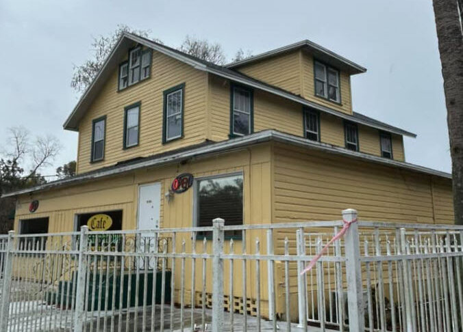 Yellow exterior of the former Masaryk Hotel, now Masaryktown Café, behind a white fence in Hernando County, Florida