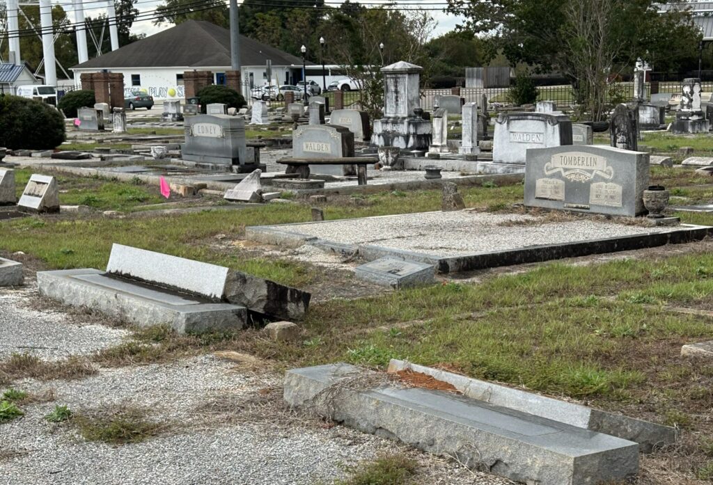 Weathered and damaged gravestones in Enterprise City Cemetery, with some markers broken or leaning among overgrown grass and gravel pathways.