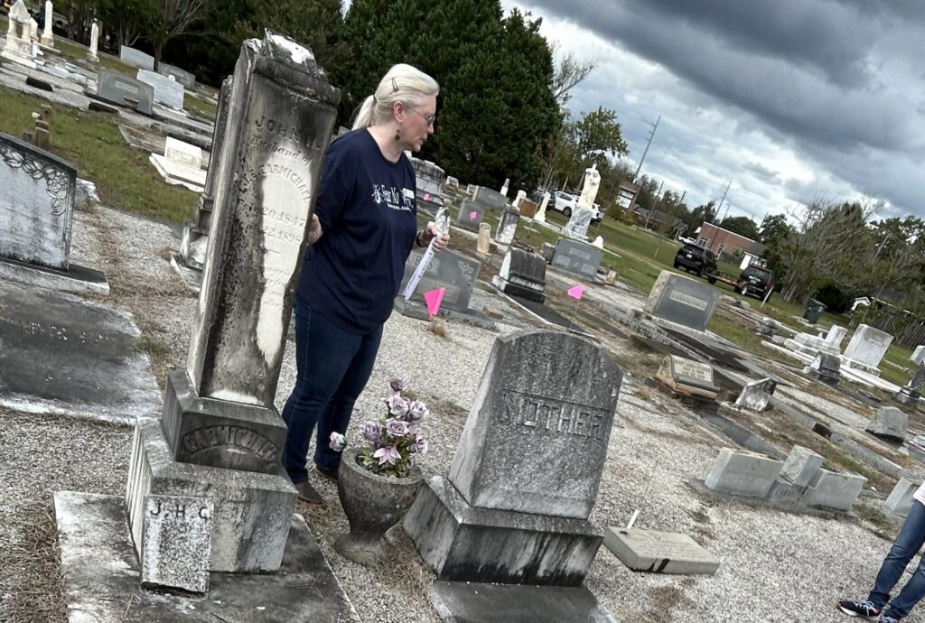 Visitor standing among historic gravestones at Enterprise City Cemetery in Alabama, pausing near a headstone while looking across the surrounding markers under cloudy skies.