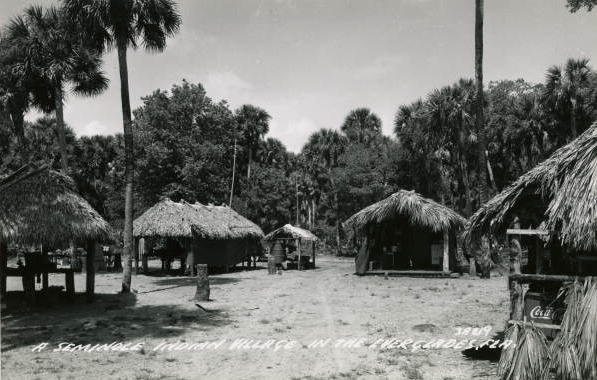 Historic Seminole chickee village in the Florida Everglades, featuring thatched-roof huts and palm trees, showing traditional Native American dwellings in a swamp environment