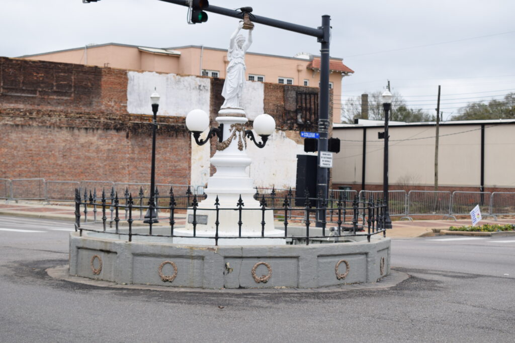 Boll Weevil Monument in downtown Enterprise, Alabama, featuring a statue of a woman holding a boll weevil above her head, surrounded by a small fenced traffic circle.