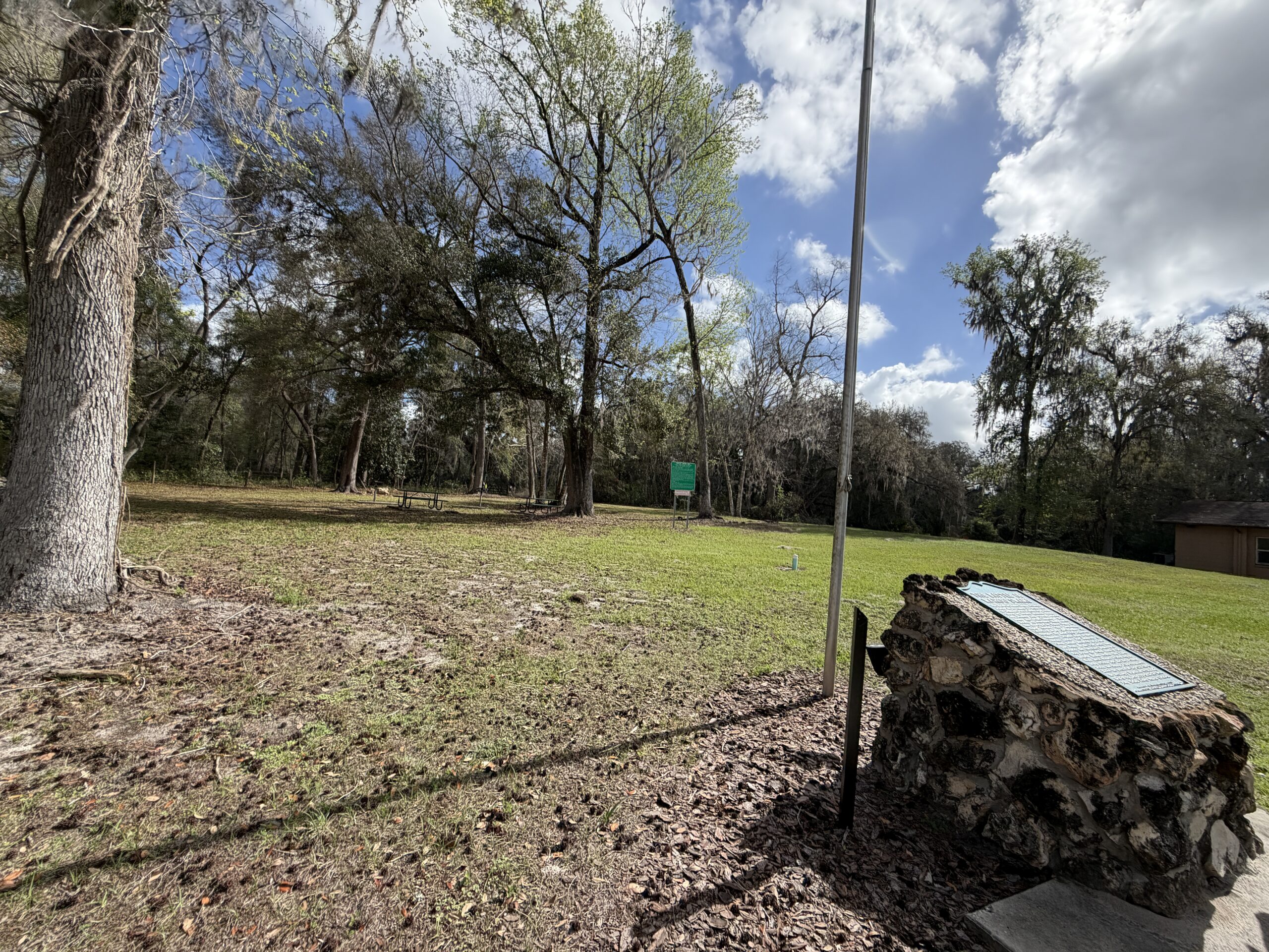Historical marker at Wahoo Swamp in Florida, surrounded by oak trees and open grassy clearing under a bright blue sky, marking the site of a key Second Seminole War battle