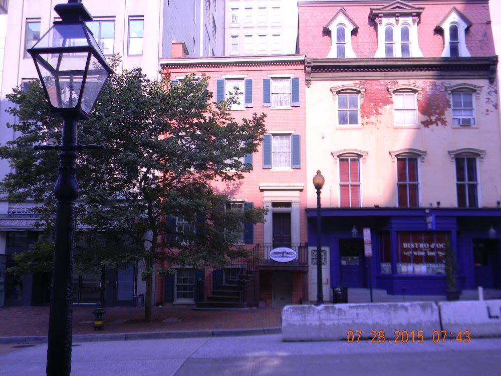 Street view of the Petersen House across from Ford’s Theatre in Washington, D.C., with a lamppost in the foreground and early morning light casting shadows on the row buildings.