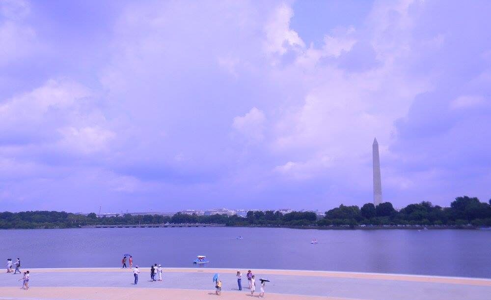 View across the Tidal Basin in Washington, D.C., with visitors along the shoreline and the Washington Monument rising in the distance.