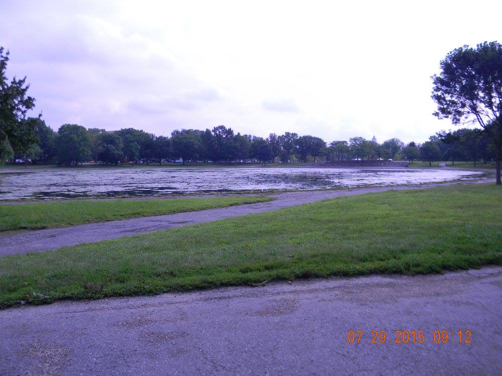 View of Constitution Gardens on the National Mall with a murky pond and the Washington Monument visible in the distance.
