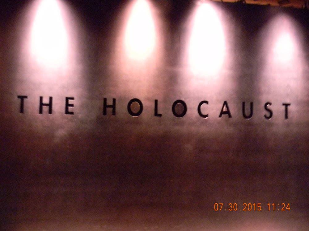 The word "Holocaust" displayed on a stone wall beneath four overhead lights inside the United States Holocaust Memorial Museum in Washington, D.C.