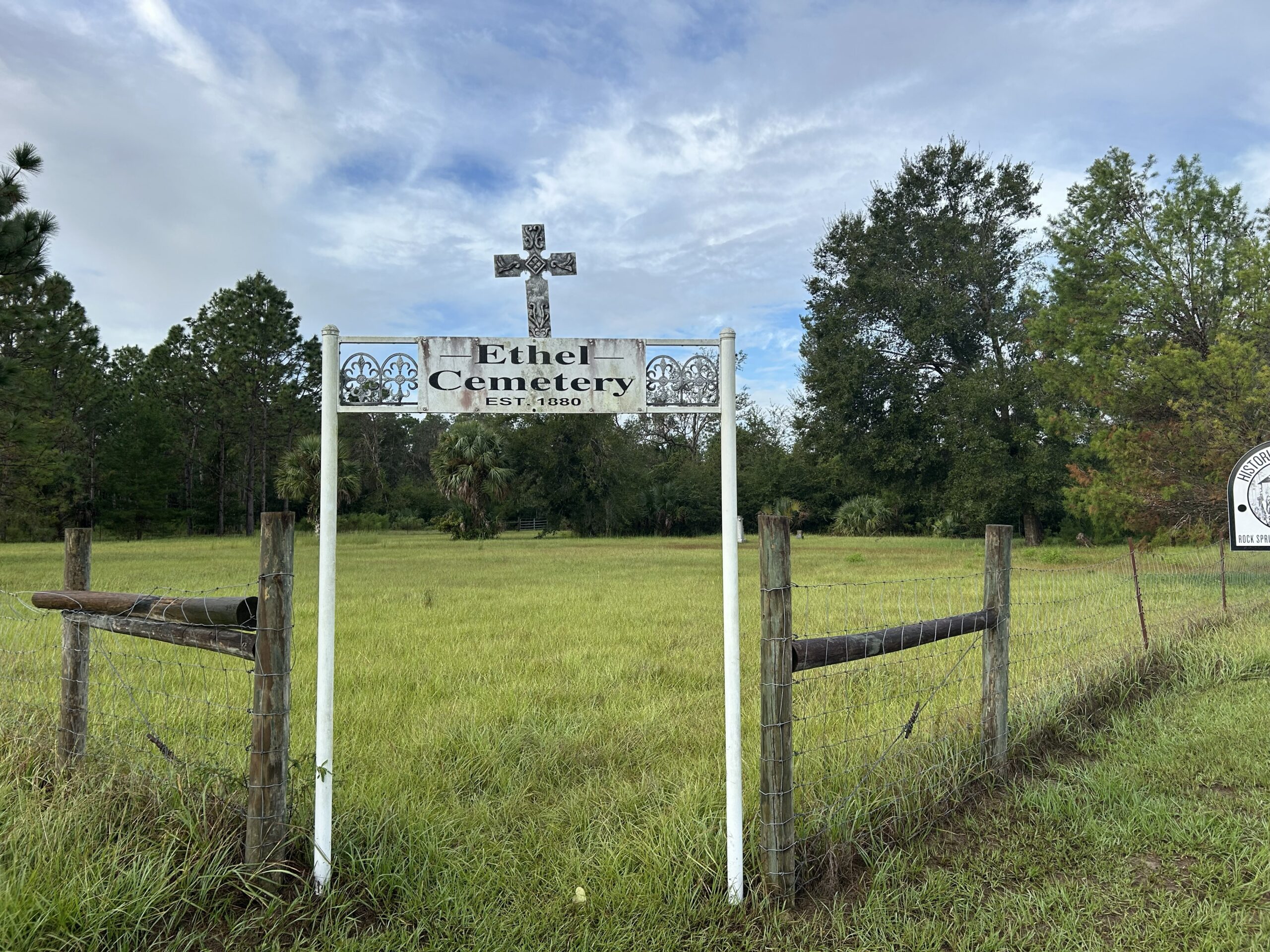 Weathered entrance sign for Ethel Cemetery, established in 1880, standing beside a grassy field within Rock Springs Run State Reserve in Florida.