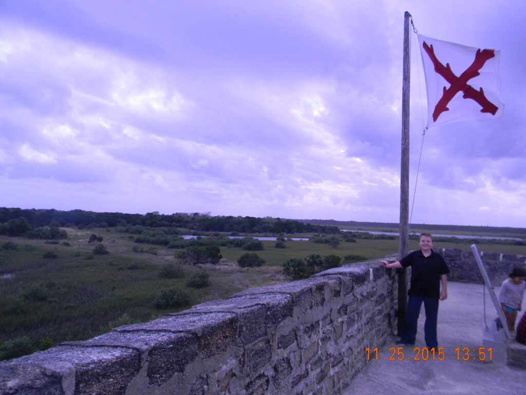My son standing beside the Spanish Cross of Burgundy flag atop Fort Matanzas, overlooking the marshes and Matanzas Inlet in Florida.