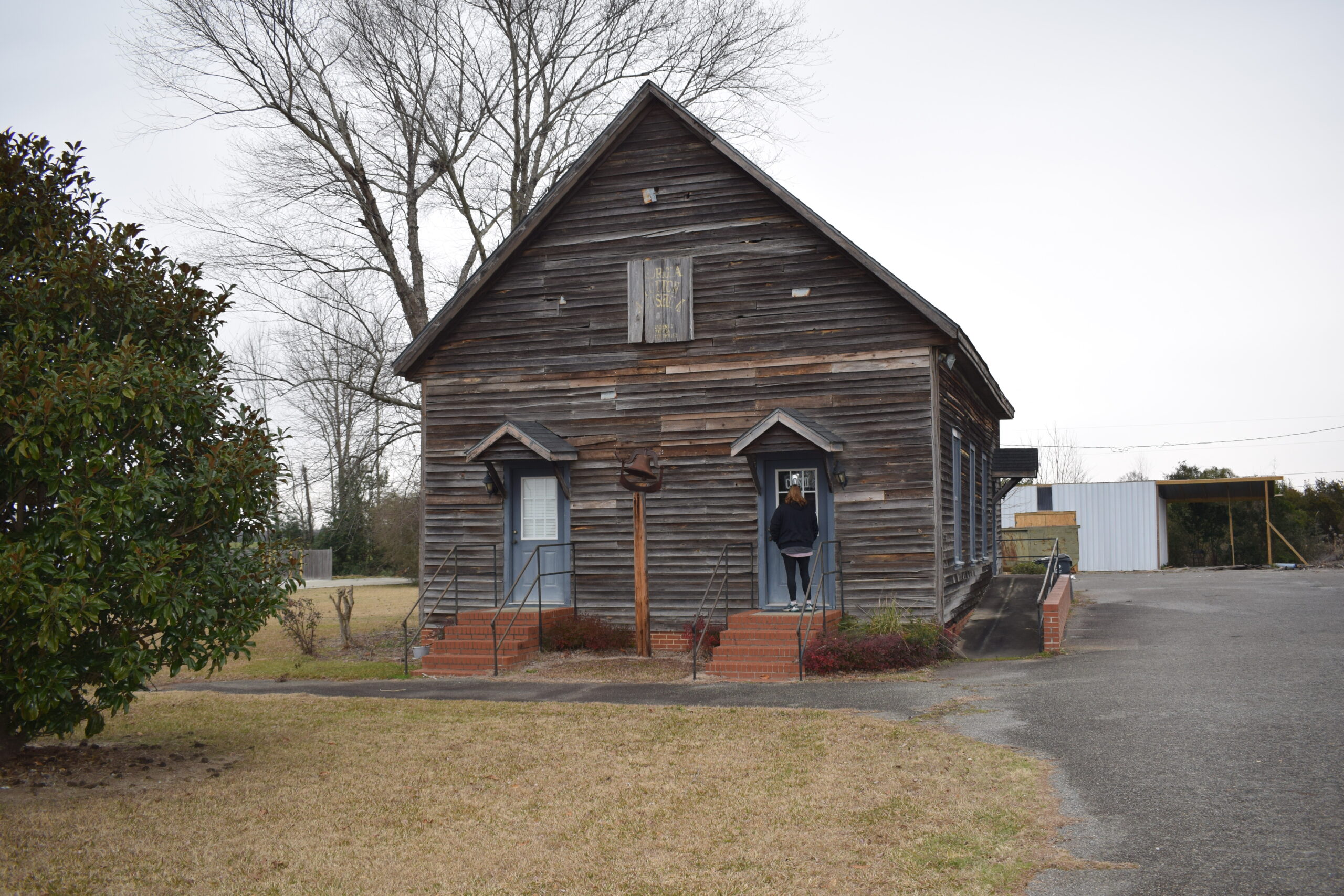 Exterior of the Georgia State Cotton Museum in Georgia with a visitor walking toward the entrance on an overcast winter day.