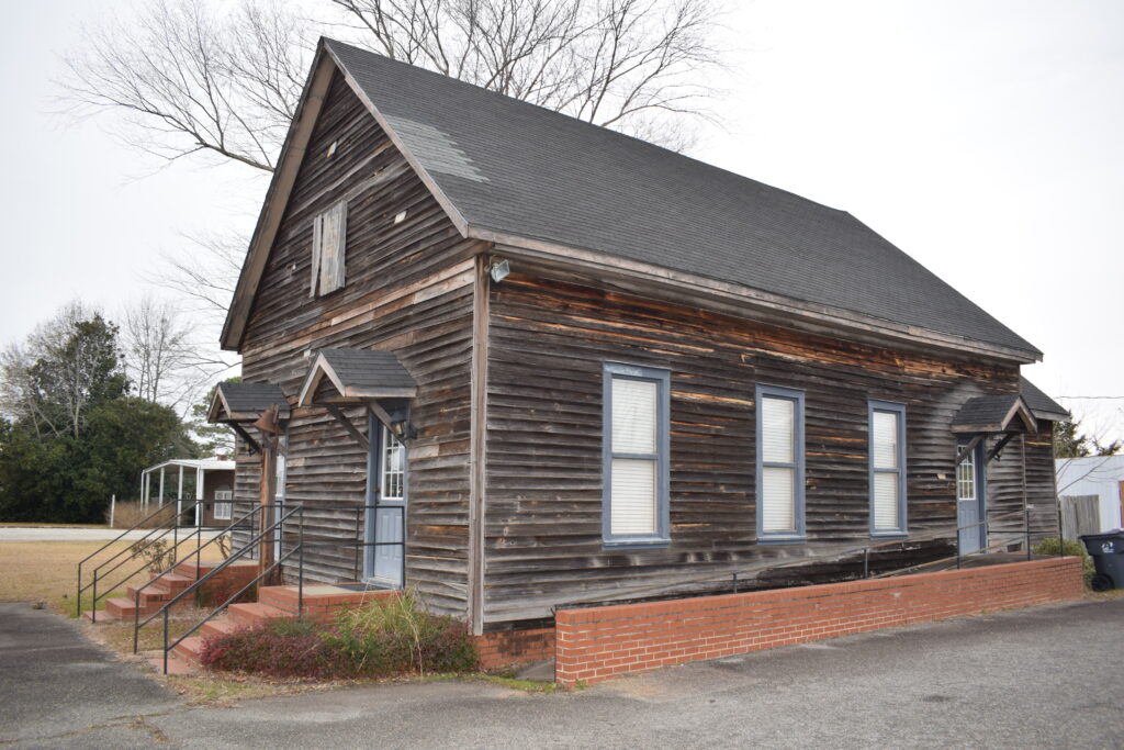 Side view of the weathered wooden Georgia State Cotton Museum building in Georgia, showcasing its rustic architecture and preserved historic character.