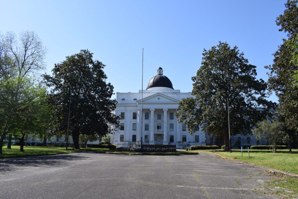 The historic Central State Hospital administration building in Milledgeville, Georgia, with its white neoclassical façade, black domed roof, and expansive grounds.