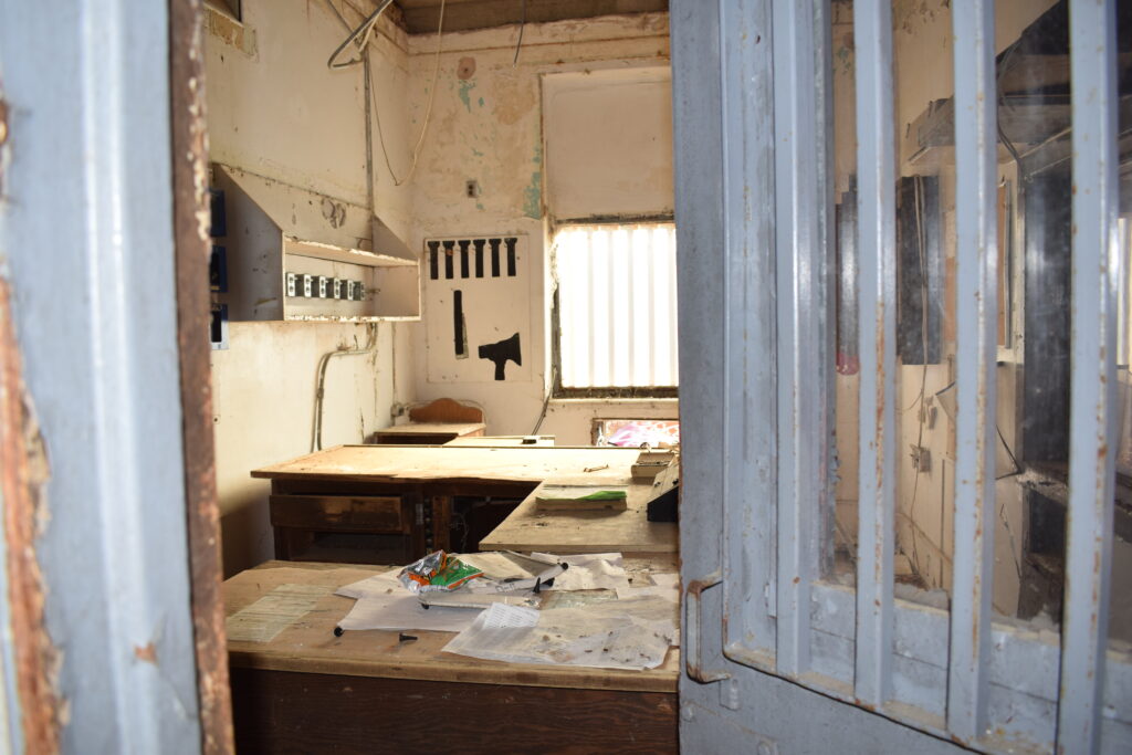 An abandoned office with desks, scattered paperwork, and barred doors inside the former Rivers State Prison in Milledgeville, Georgia.
