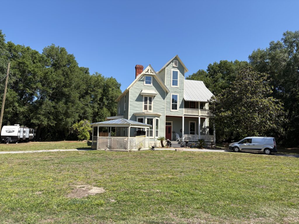 The restored Thomas R. Ayer House, a historic Queen Anne-style Victorian home in Oklawaha, Florida, viewed from the front lawn on a clear sunny day.