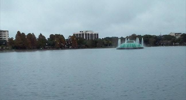 The iconic Lake Eola Fountain rises from the center of the lake with the downtown Orlando skyline and shoreline visible in the background.
