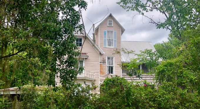 The Thomas R. Ayer House in Oklawaha, Florida, partially hidden by trees before its restoration, showing the historic Queen Anne home weathered by time.