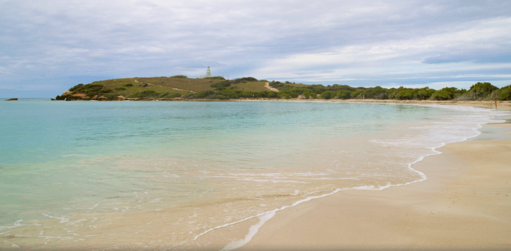 Curving sandy shoreline and turquoise water at Playa Sucia with Los Morrillos Lighthouse in the distance in Cabo Rojo, Puerto Rico.