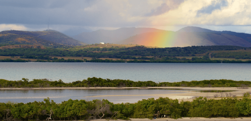 Rainbow glowing beneath storm clouds over the hills and coastal wetlands of Cabo Rojo, Puerto Rico.