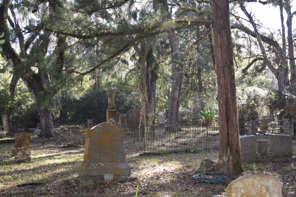 Weathered headstones and iron-fenced family plots beneath old trees at Micanopy Historic Cemetery in Florida