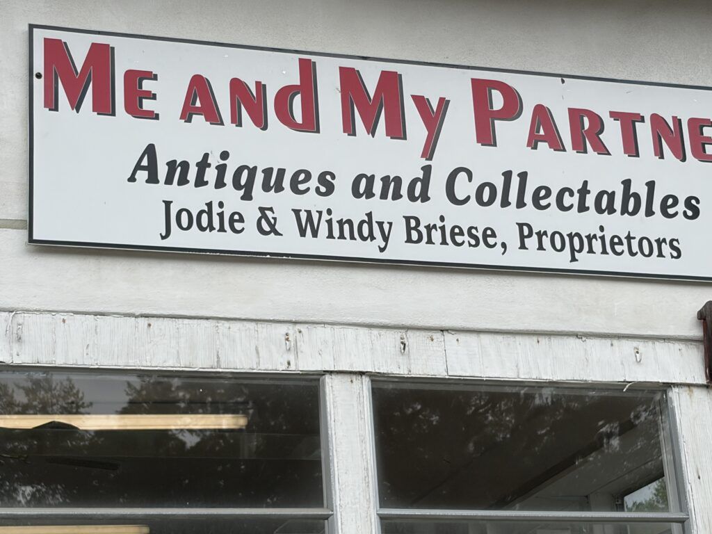Me and My Partner Antiques and Collectibles sign naming Jodie and Windy Briese as proprietors in Woodbine, Georgia