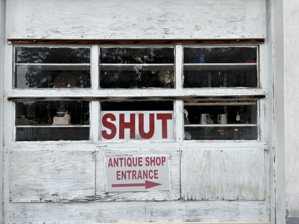 SHUT sign in the window of Dead People’s Things for Sale with antiques still visible inside the Woodbine, Georgia shop