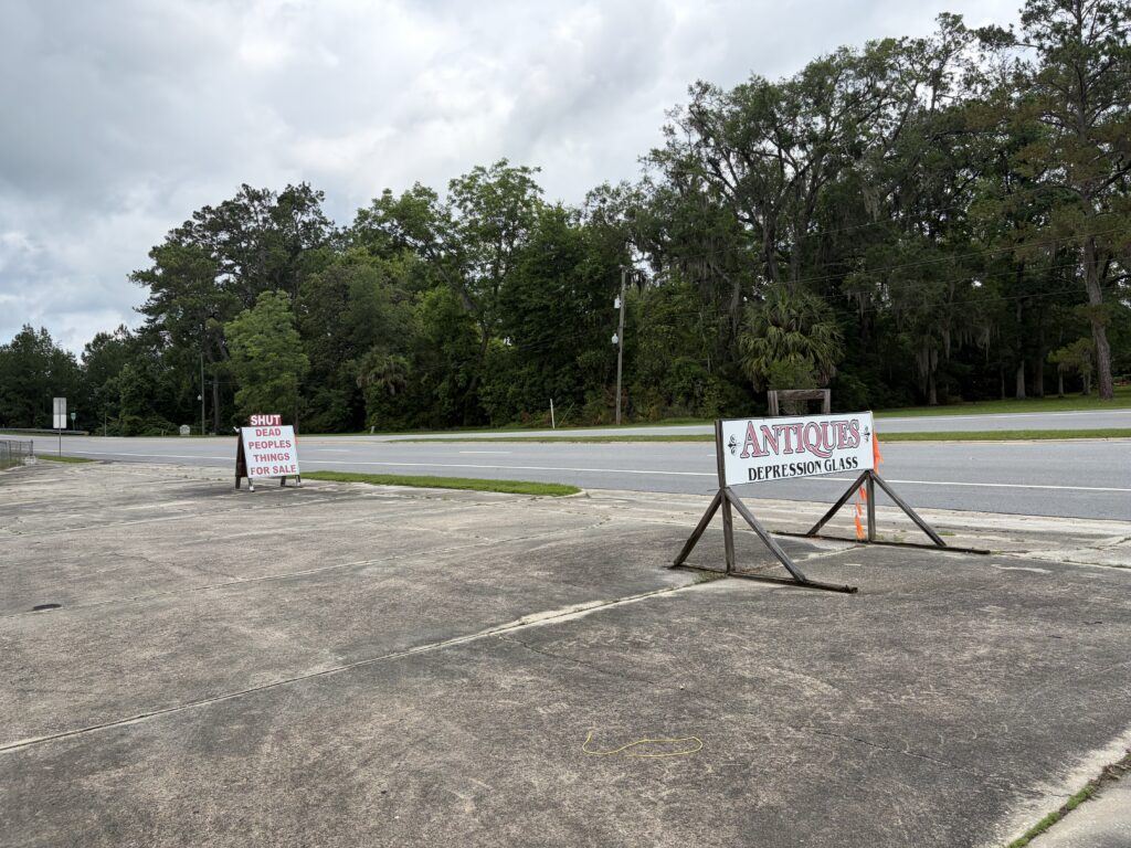 Dead People’s Things for Sale and antiques signs standing beside an empty parking lot along U.S. Highway 17 in Woodbine, Georgia