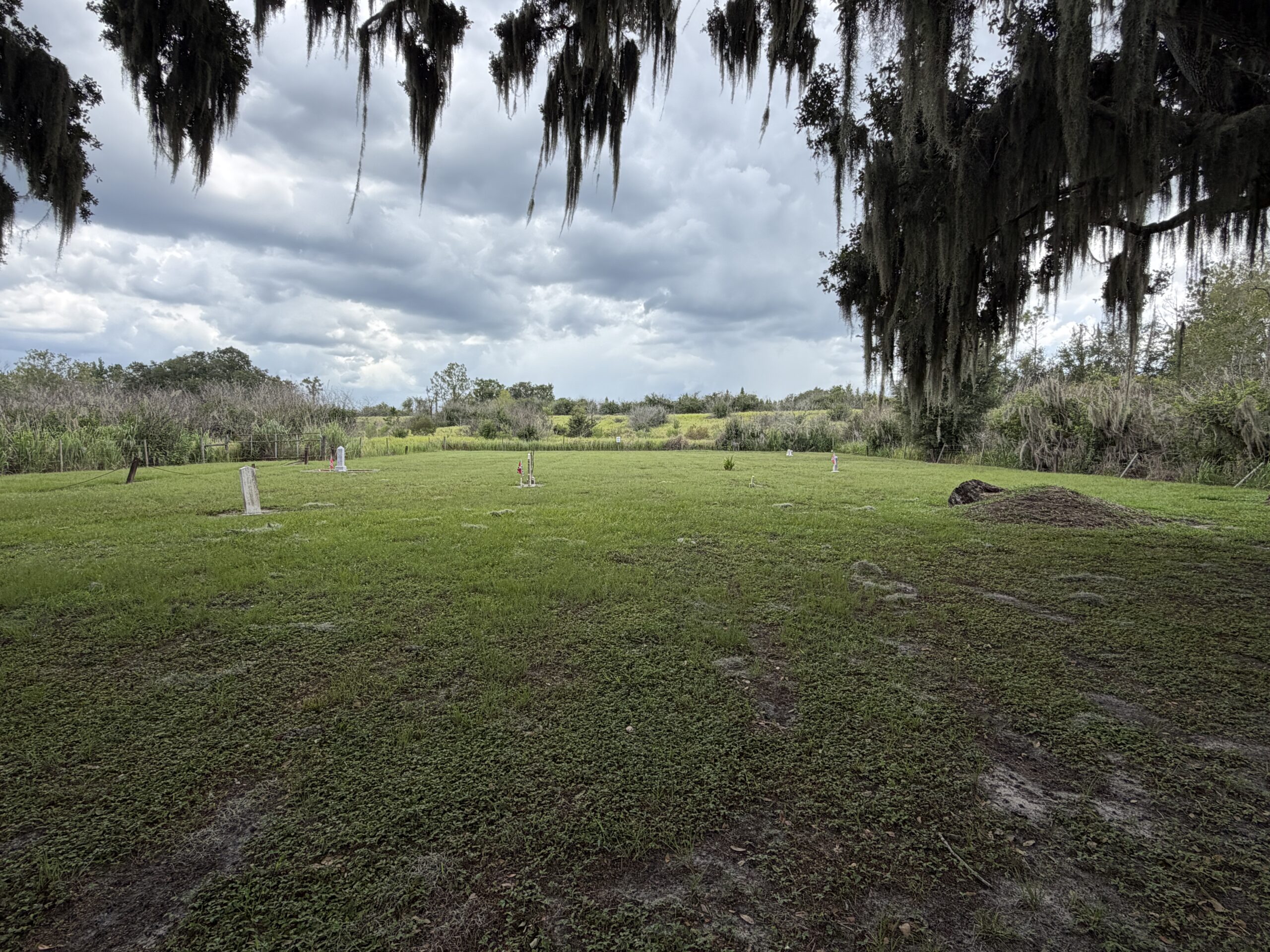 Weathered gravestones at Crum-Durrance Cemetery beneath Spanish moss and storm clouds in Polk County, Florida.