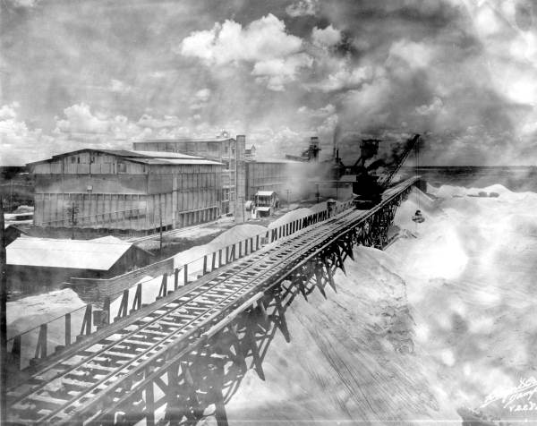 Historic photograph of a phosphate mining operation in Brewster, Florida, with industrial buildings, conveyor equipment, and large piles of phosphate material.