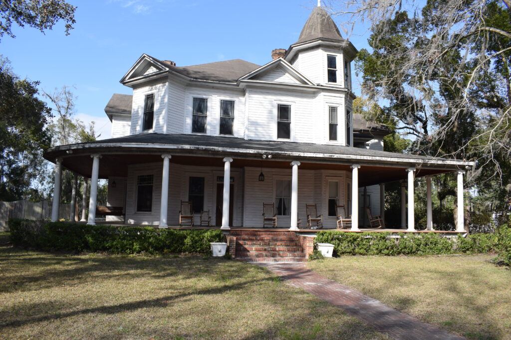 Large historic white home with a wraparound porch and tower in White Springs, Florida.
