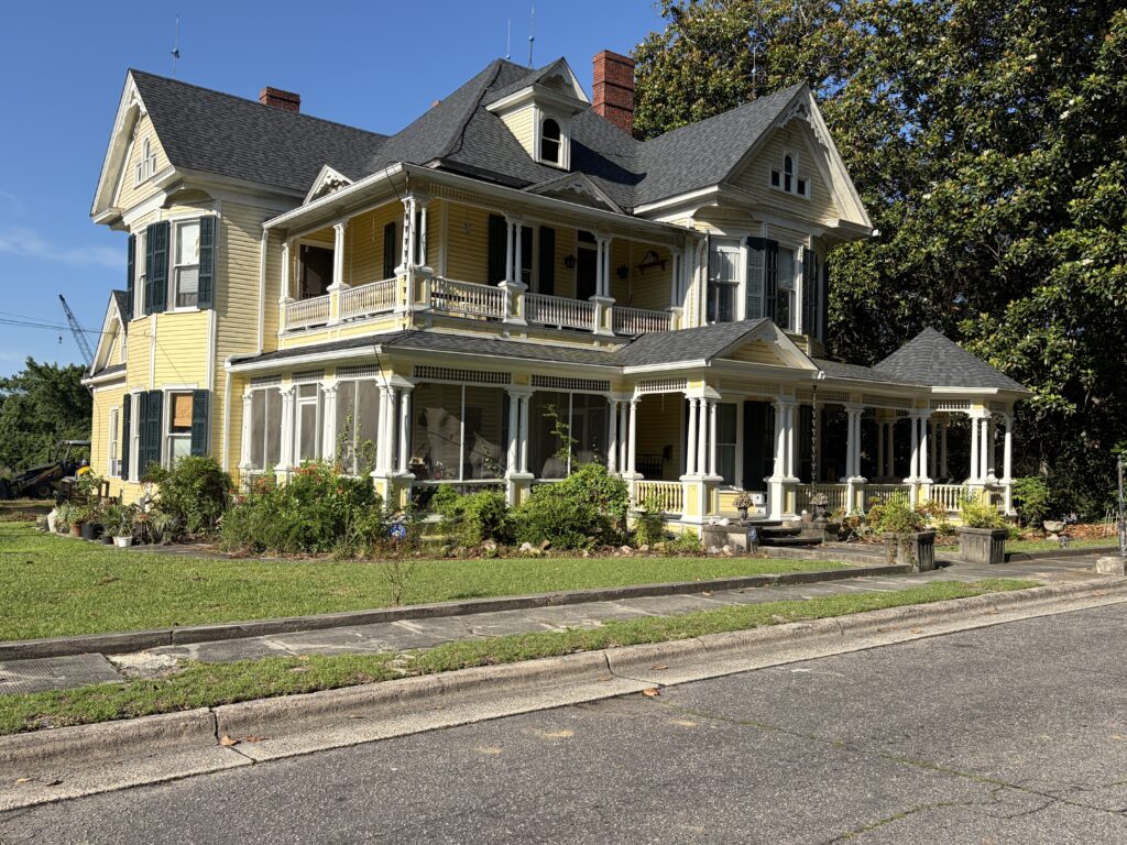 Luther Henry Caldwell House as seen from the street during our visit to Lumberton, North Carolina, with its yellow exterior and elaborate porches.