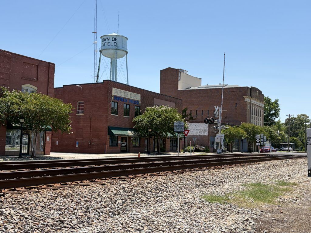 Railroad tracks running through historic downtown Enfield, North Carolina, with brick buildings and the Town of Enfield water tower behind them.