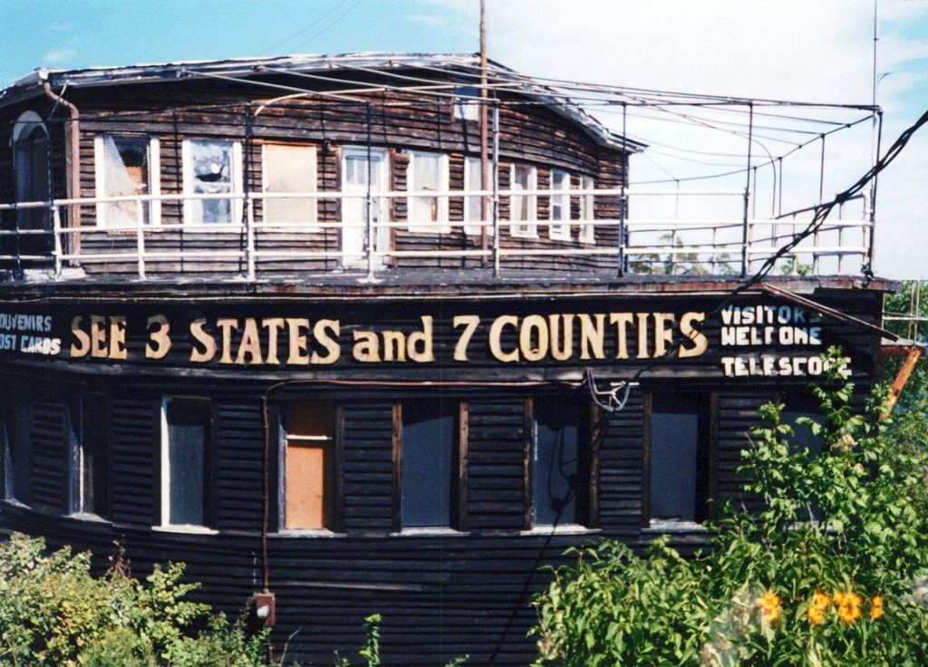 Color photograph of the abandoned Grand View Ship Hotel in Pennsylvania, showing weathered wooden siding, damaged windows, rusting observation deck railings, and overgrown vegetation.