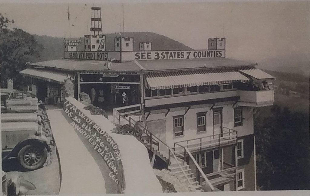 Historic black-and-white photograph of the original Grand View Point Hotel along Pennsylvania’s Lincoln Highway, featuring castle-style rooftop towers, striped awnings, and a sign advertising views of three states and seven counties.